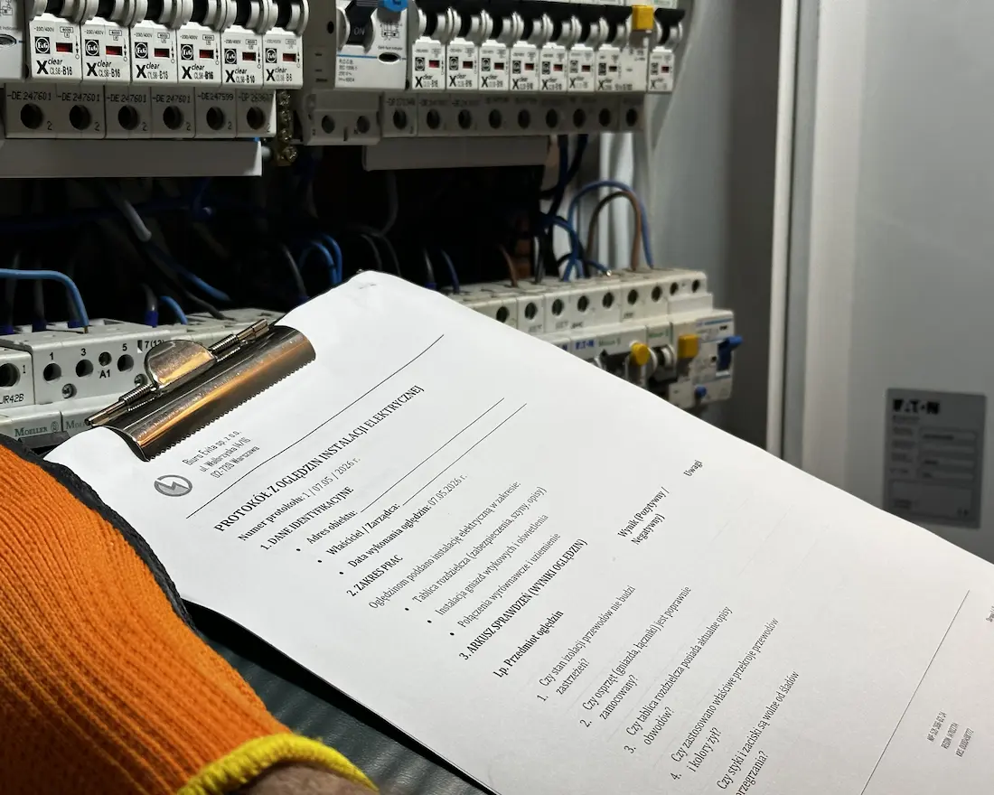 Elektryk wypełnia protokół oględzin instalacji elektrycznej przy rozdzielnicy w Warszawie