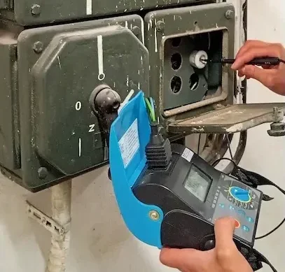 Pomiary starej instalacji elektrycznej w żeliwnej rozdzielnicy podczas przeglądu technicznego.