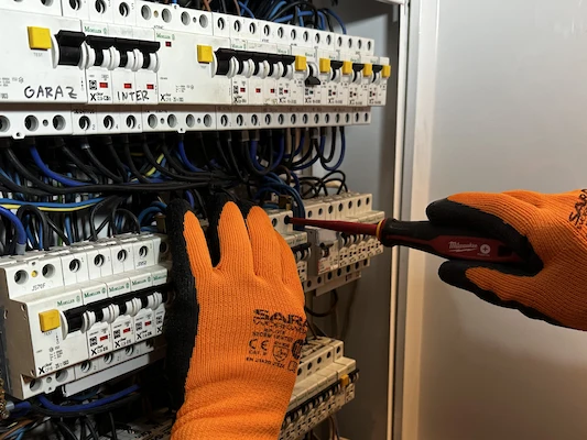 Elektryk wykonuje przegląd i konserwację domowej rozdzielnicy elektrycznej w celu zapewnienia bezpieczeństwa instalacji.